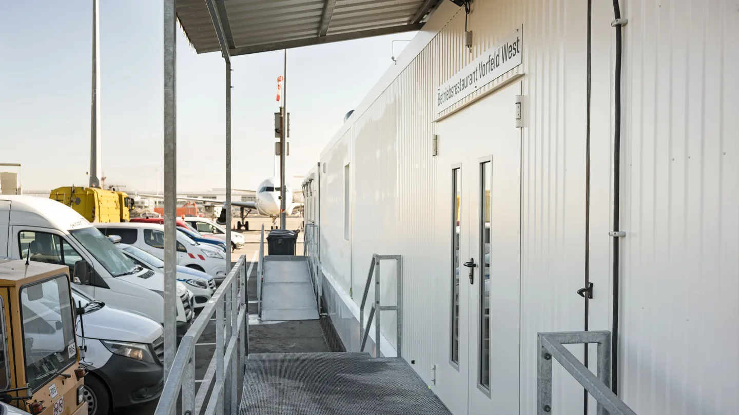 Überdachter Zugang zur Interimskantine, daneben Einsatzfahrzeuge des Flughafens.