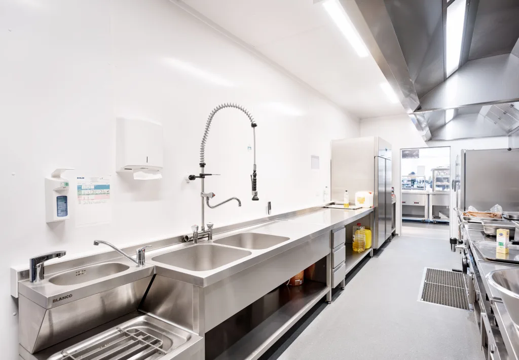 Spülbereich im Küchencontainer: Edelstahlbecken mit Vorspülbrause und durchgehender Arbeitszeile.